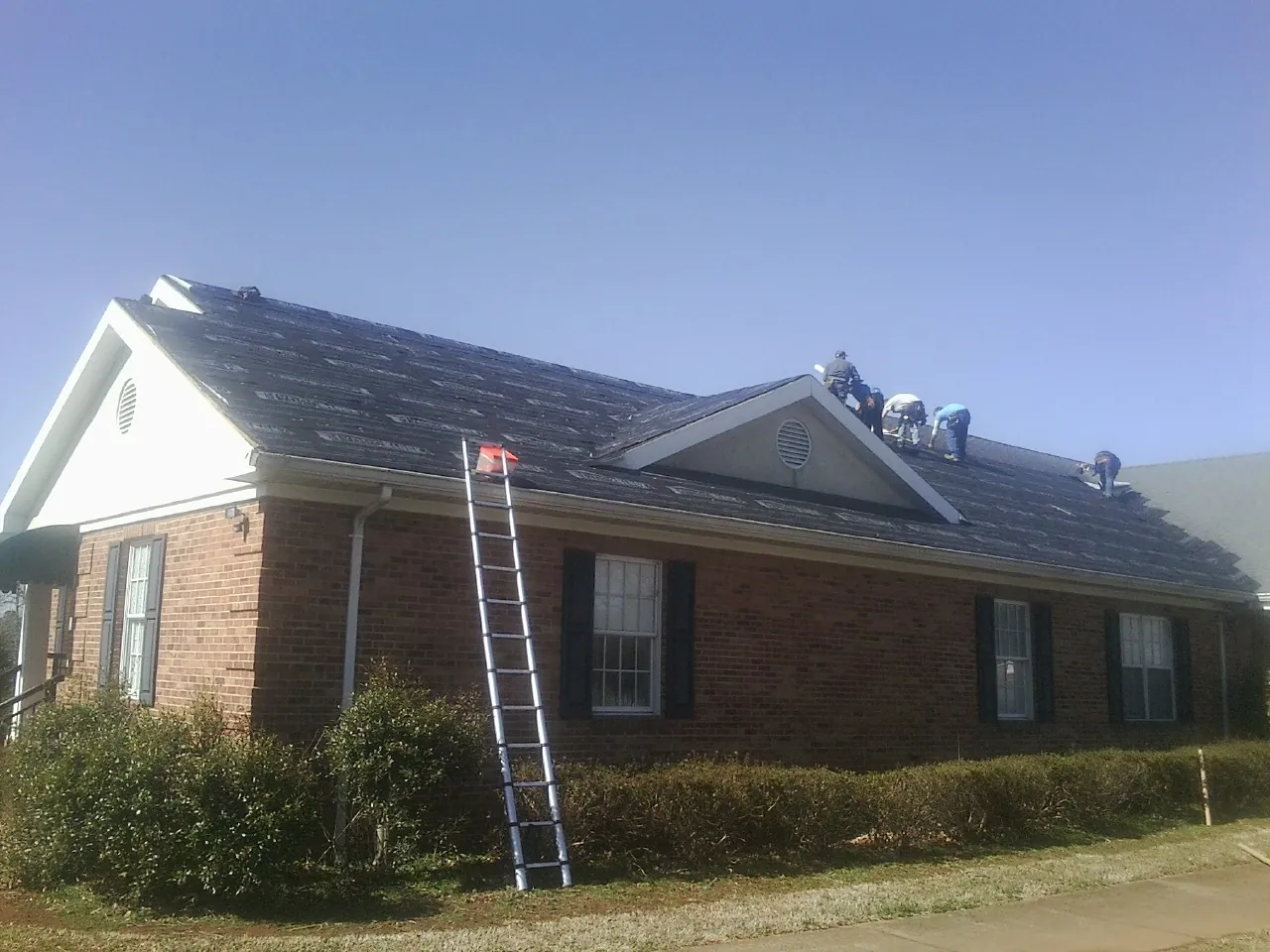 Crew tearing shingles off a brick ranch roof with a ladder set — Emergency Roof Repair work by our crew in North Bend